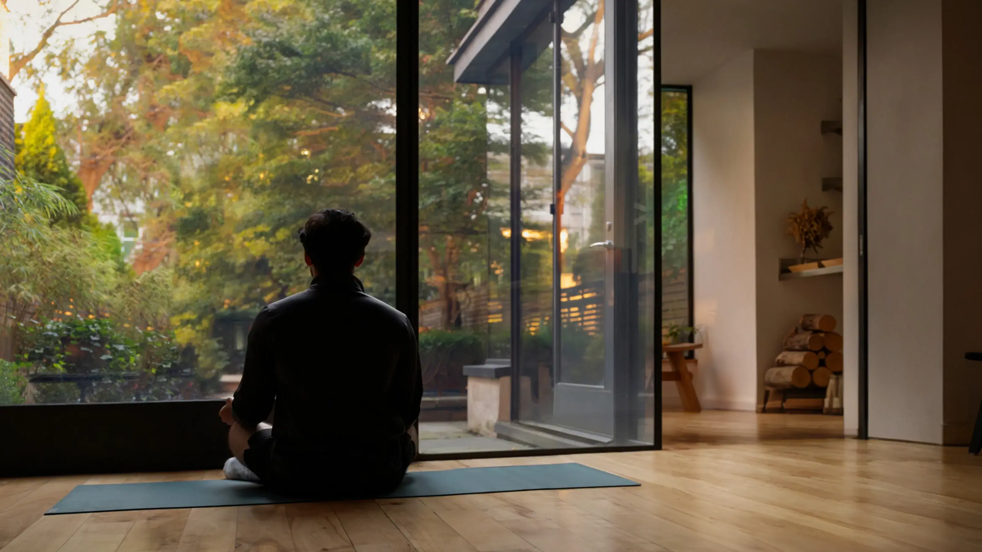 A person meditating by a floor-to-ceiling window at dusk