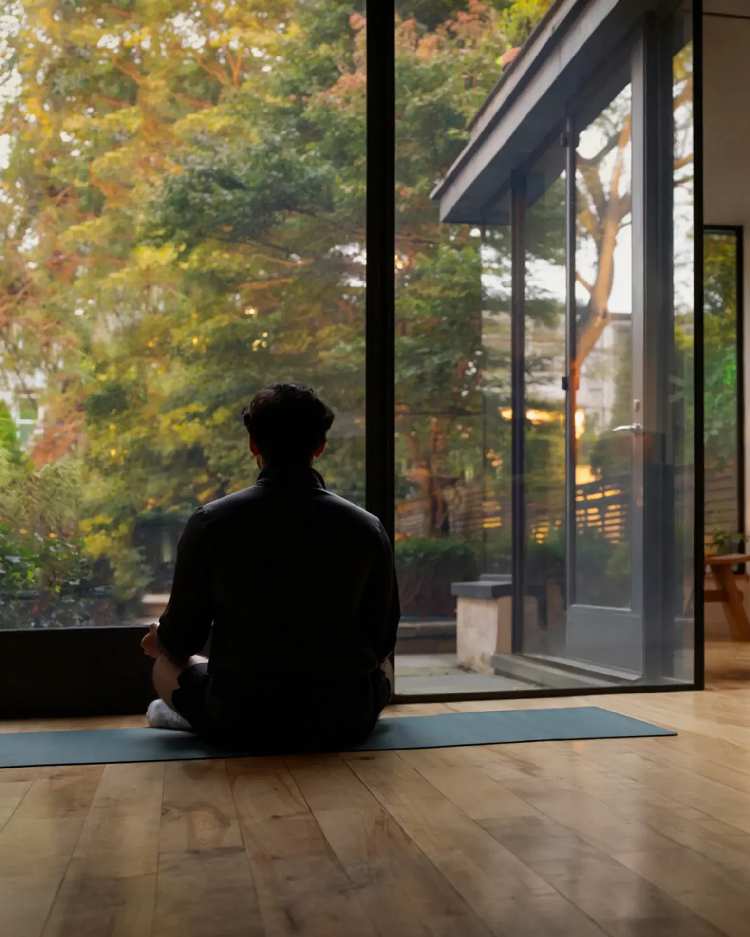 A person meditating by a floor-to-ceiling window at dusk